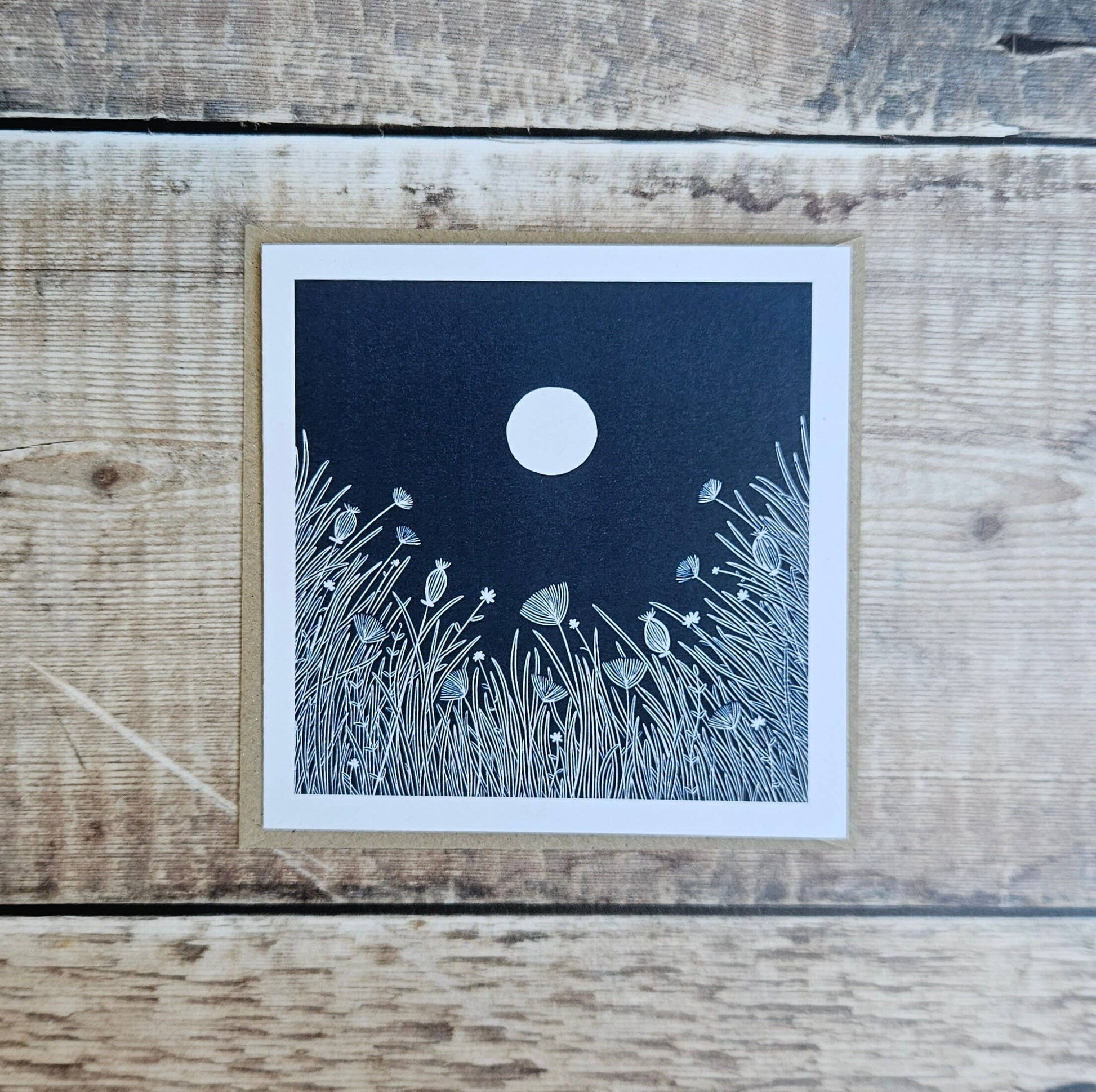 Card with a moon and grass design on a wooden surface