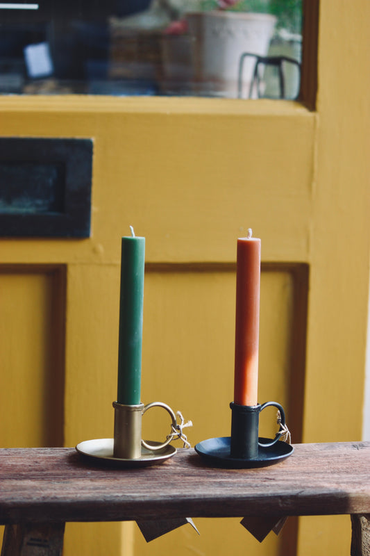 Two candles in iron candle holders on a wooden surface with a yellow wall in the background