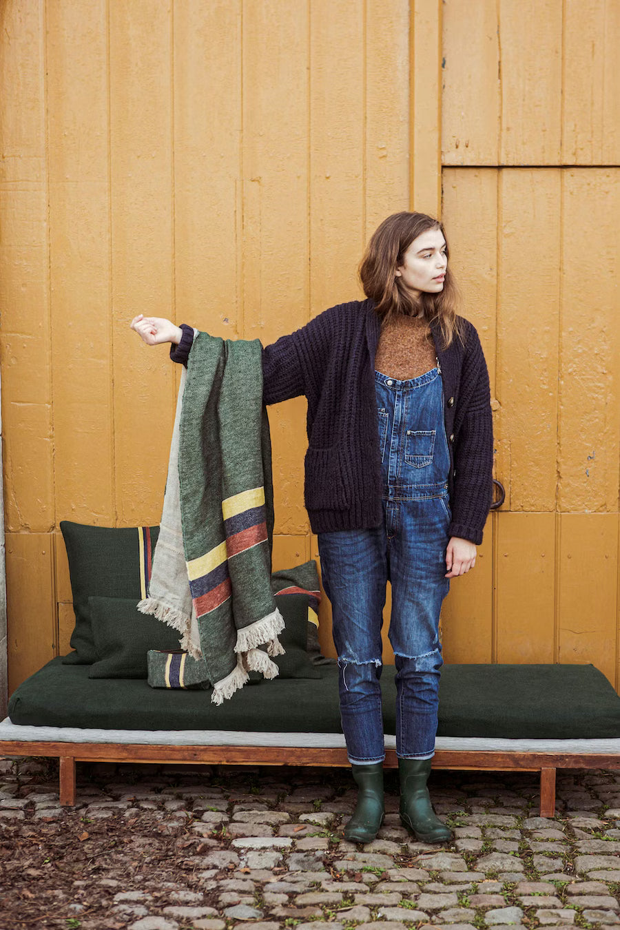 Woman holding a patterned blanket against a wooden wall. Libeco - The Belgian Towel Fouta 100% Linen