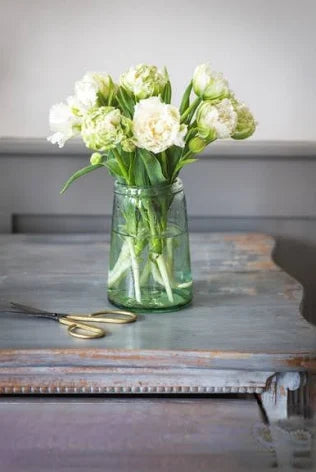 Green glass vase with white flowers on a wooden surface